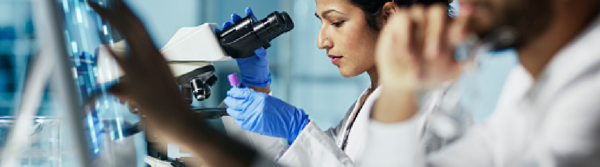 woman wearing latex gloves looking into a microscope