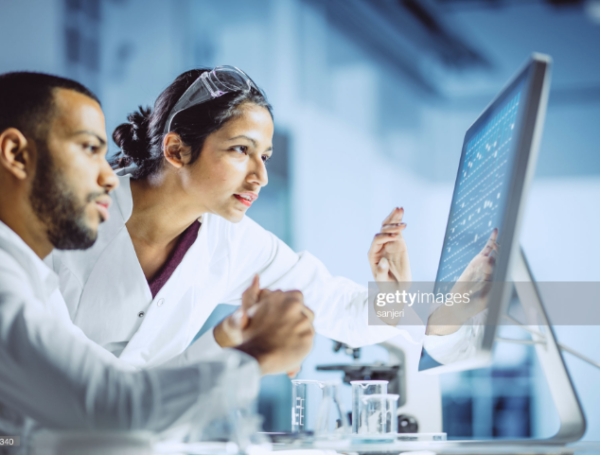 two people in lab coats looking at computer screen