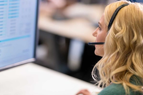 Adult woman with a headset, with a microphone, using a computer while talking to a customer in a call center.